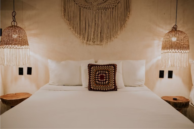 Habitacio pareja Feng Shu una cama con una pared detras, dos lamparas iguales a los lados, dos mesitas de noche iguales a los lados y colores claros en beige y arena